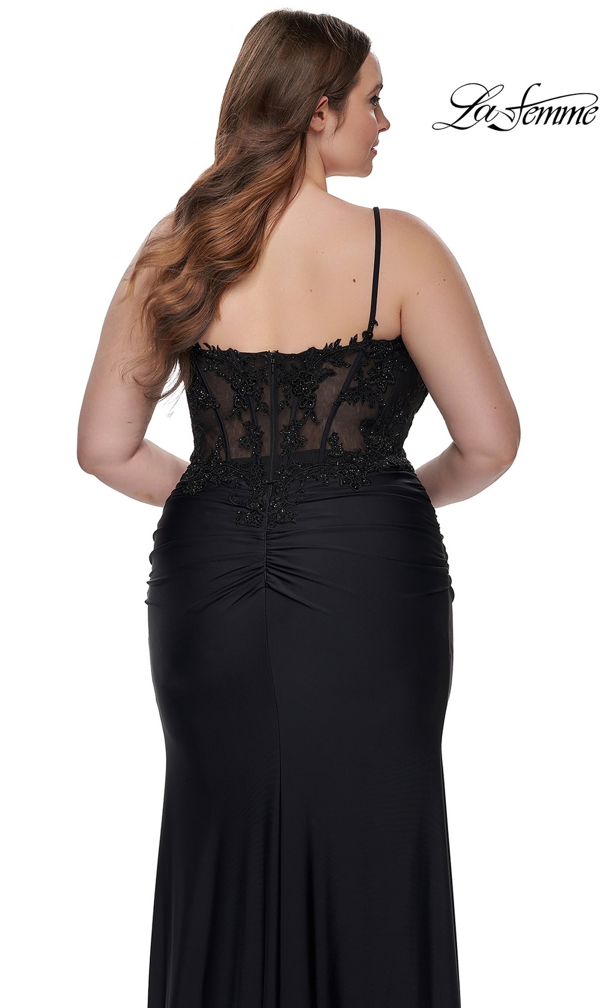 A woman wearing the La Femme Plus-Size Long Black Prom Dress 32226, featuring an embroidered-lace bodice and sheer details, stands with her back to the camera. The